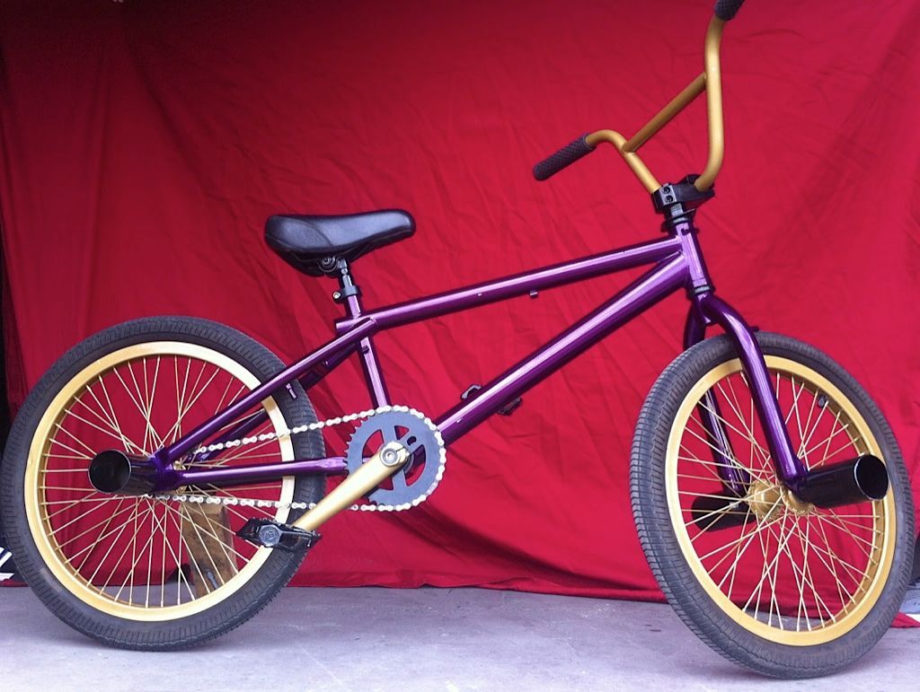 Un vélo BMX violet et or est garé devant un tissu rouge