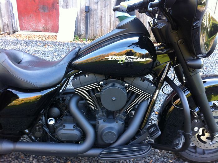 Une moto Harley Davidson noire est garée sur du gravier