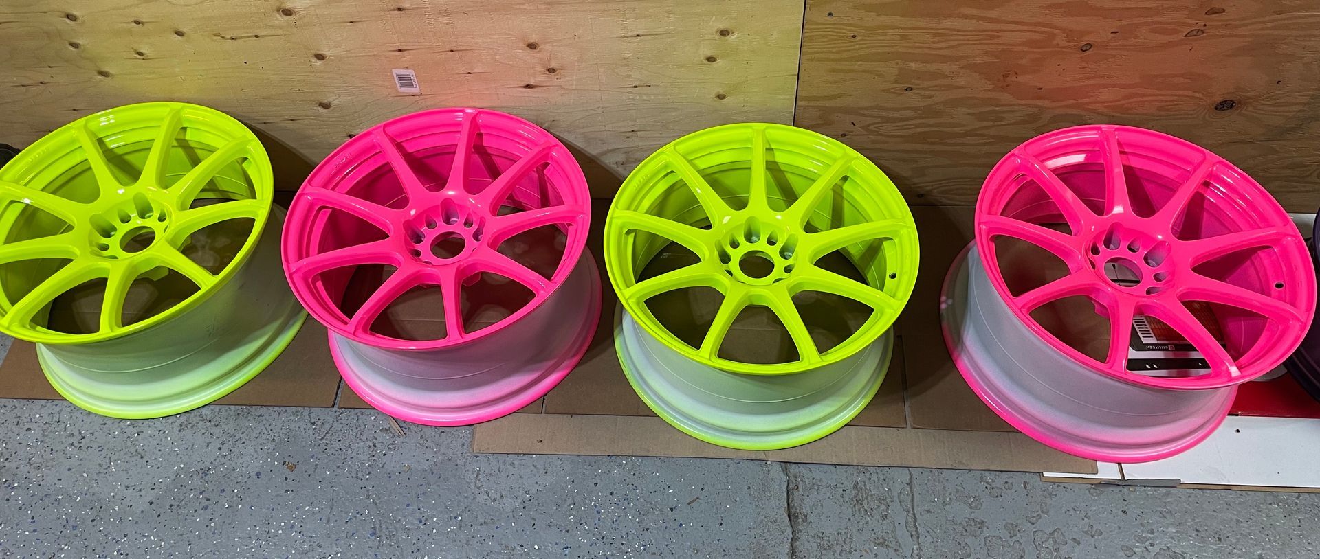 Une rangée de roues rose fluo et jaune fluo repose sur un sol en béton.