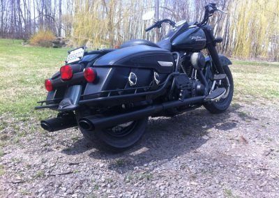 Une moto Harley Davidson noire est garée dans un champ herbeux.