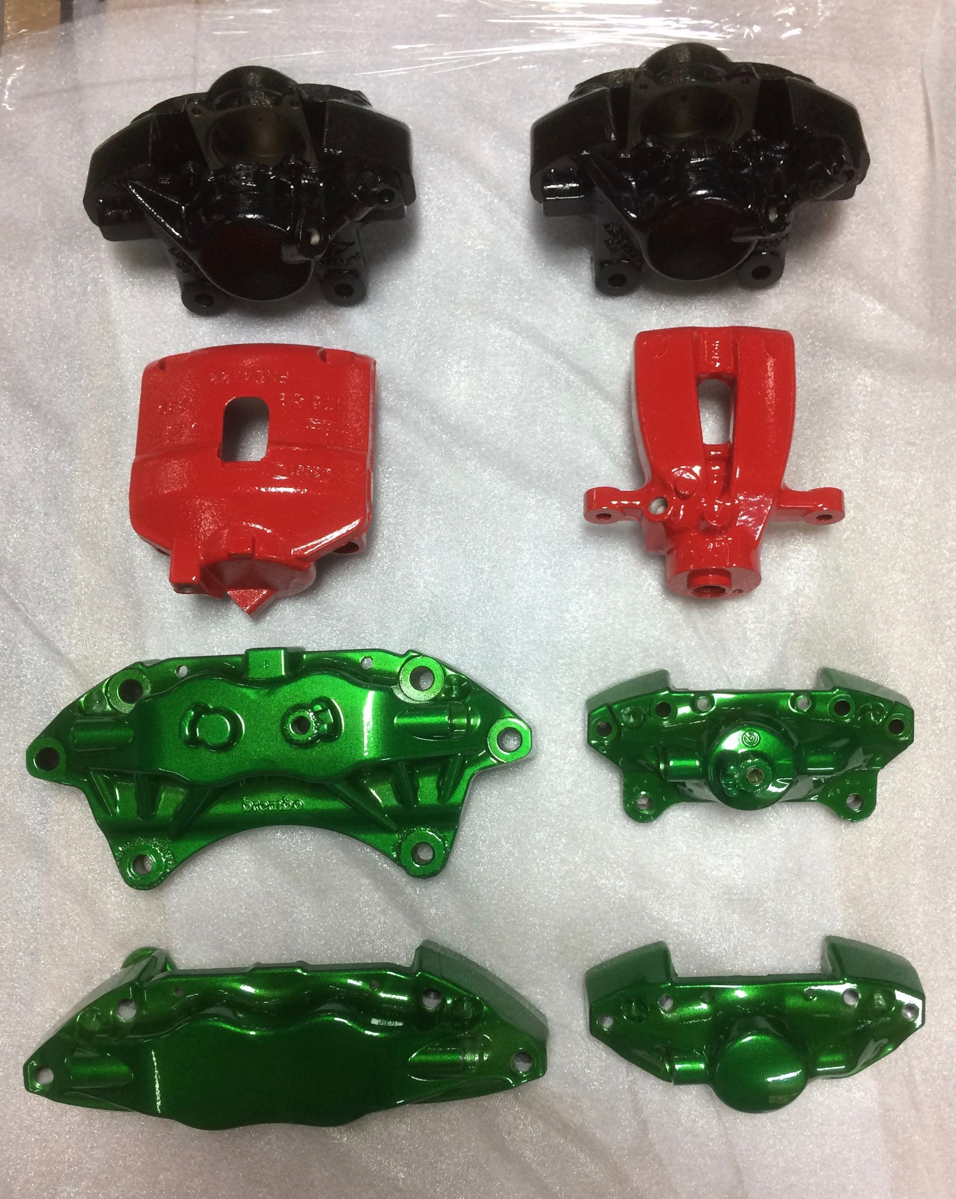 Un étrier de frein rouge, vert et noir repose sur une surface blanche.