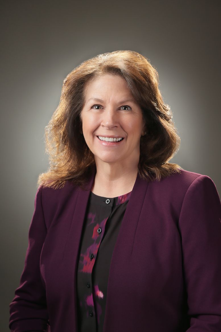 A woman is wearing a purple jacket and smiling for the camera.