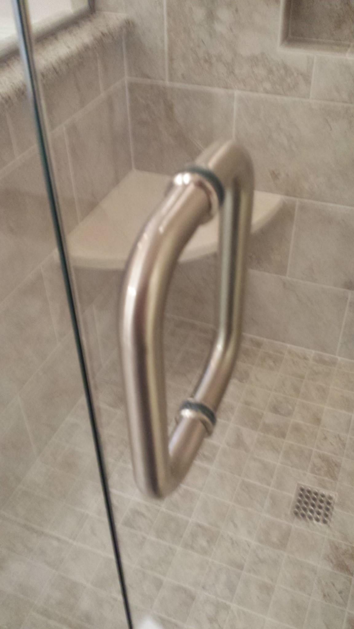 A close up of a shower door with a stainless steel handle