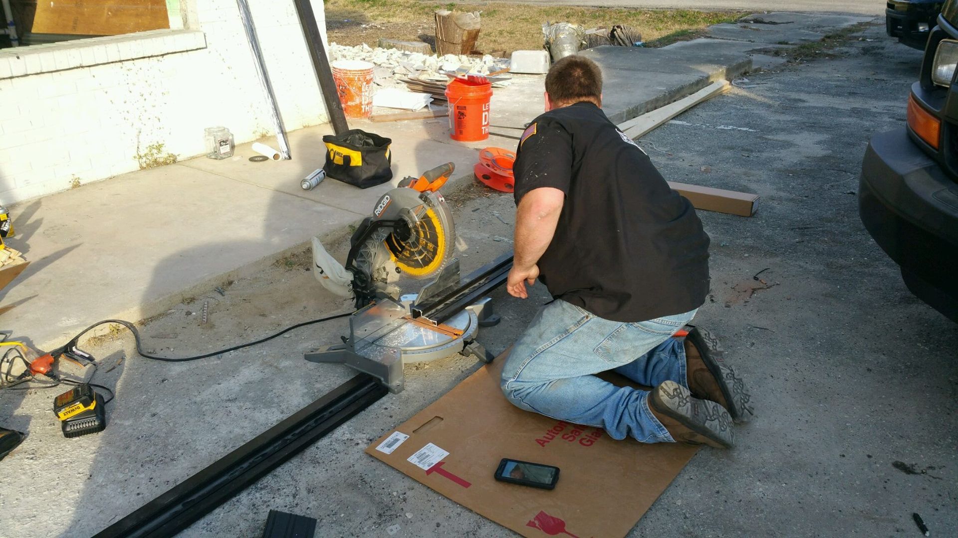 A man is kneeling down in front of a circular saw cutting a piece of wood