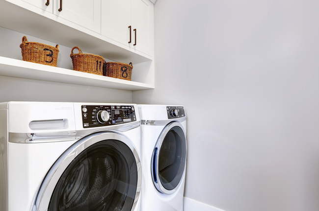 A laundry room with a washer and dryer and baskets on the shelves.