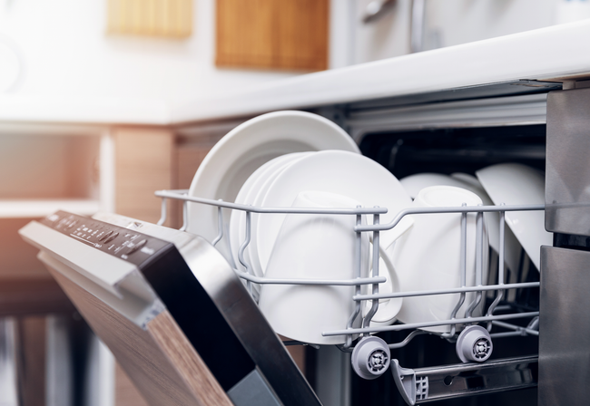 A dishwasher is filled with plates and bowls in a kitchen.