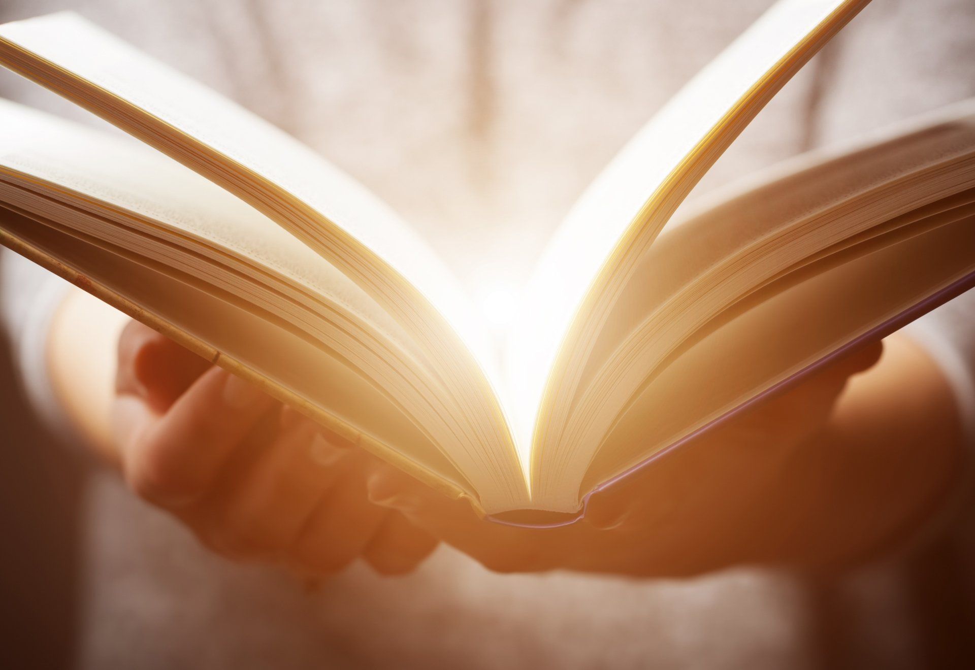 Stock picture of a person holding an open book with light glowing between the pages
