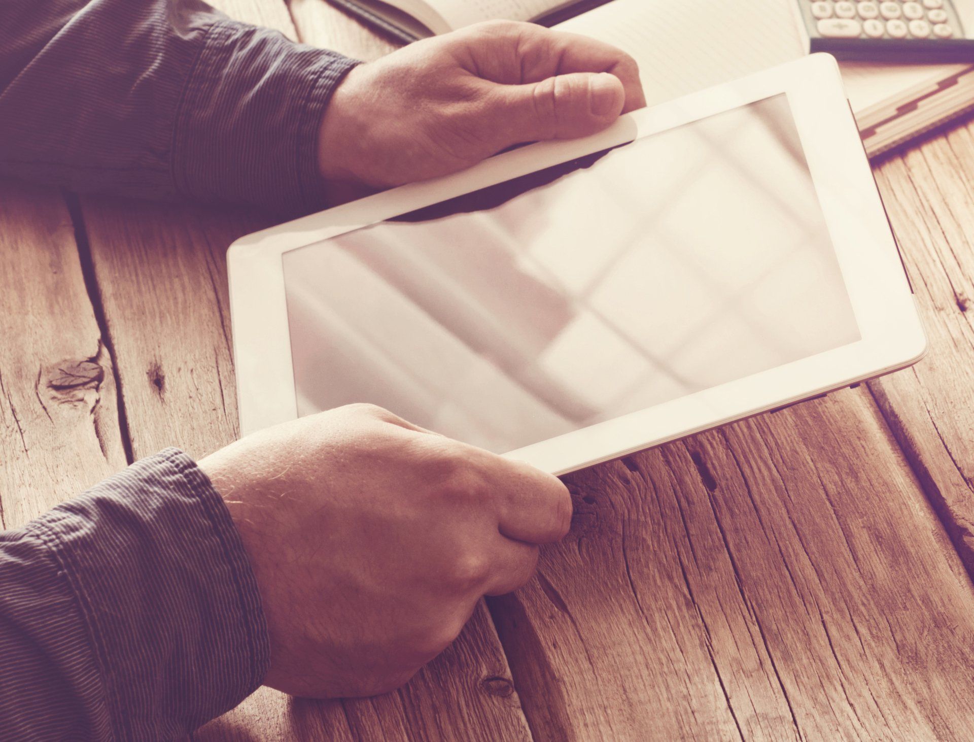 Stock picture of a person holding a tablet while sitting at a rustic table
