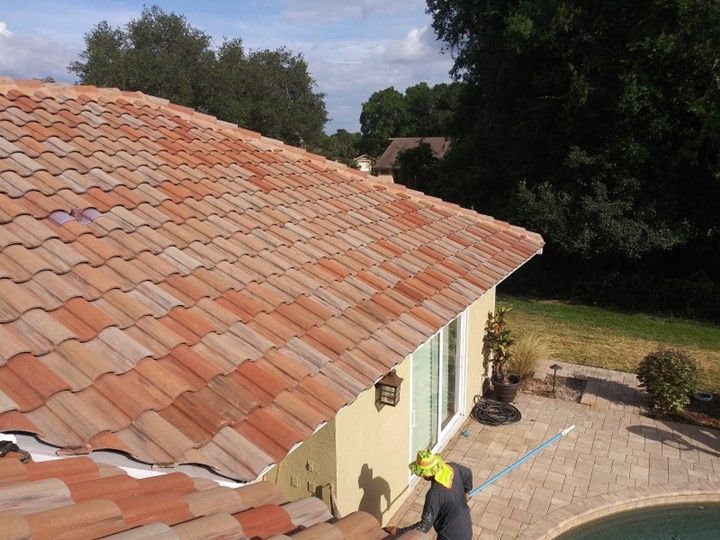 A man is cleaning the roof of a house next to a pool — Tampa, FL — Bill Shields Roofing