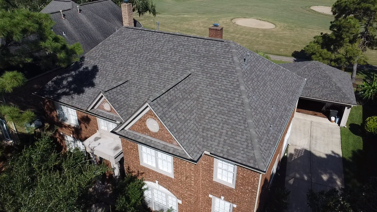 An aerial view of a large brick house with a gray roof surrounded by trees.