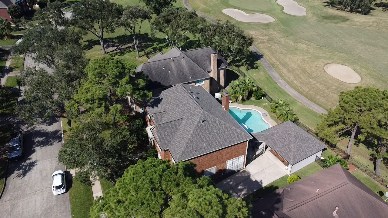 An aerial view of a house with a pool and a golf course in the background.