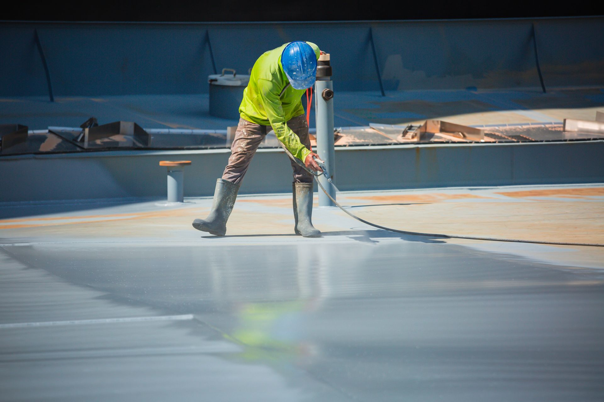 Worker applying a protective roof coating with a spray hose on a flat rooftop