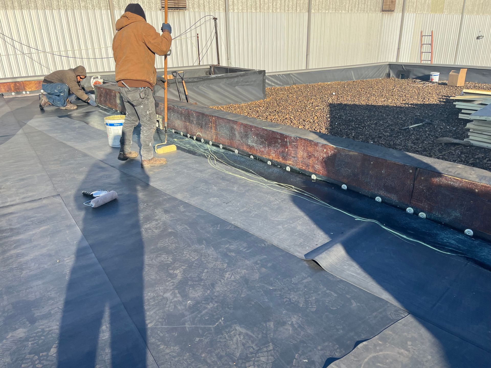 Roofing crew installing EPDM rubber roofing membrane, applying adhesive and securing seams on a comm