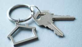 A silver keychain with two silver keys and a silver silhouette of a house on a blue background.