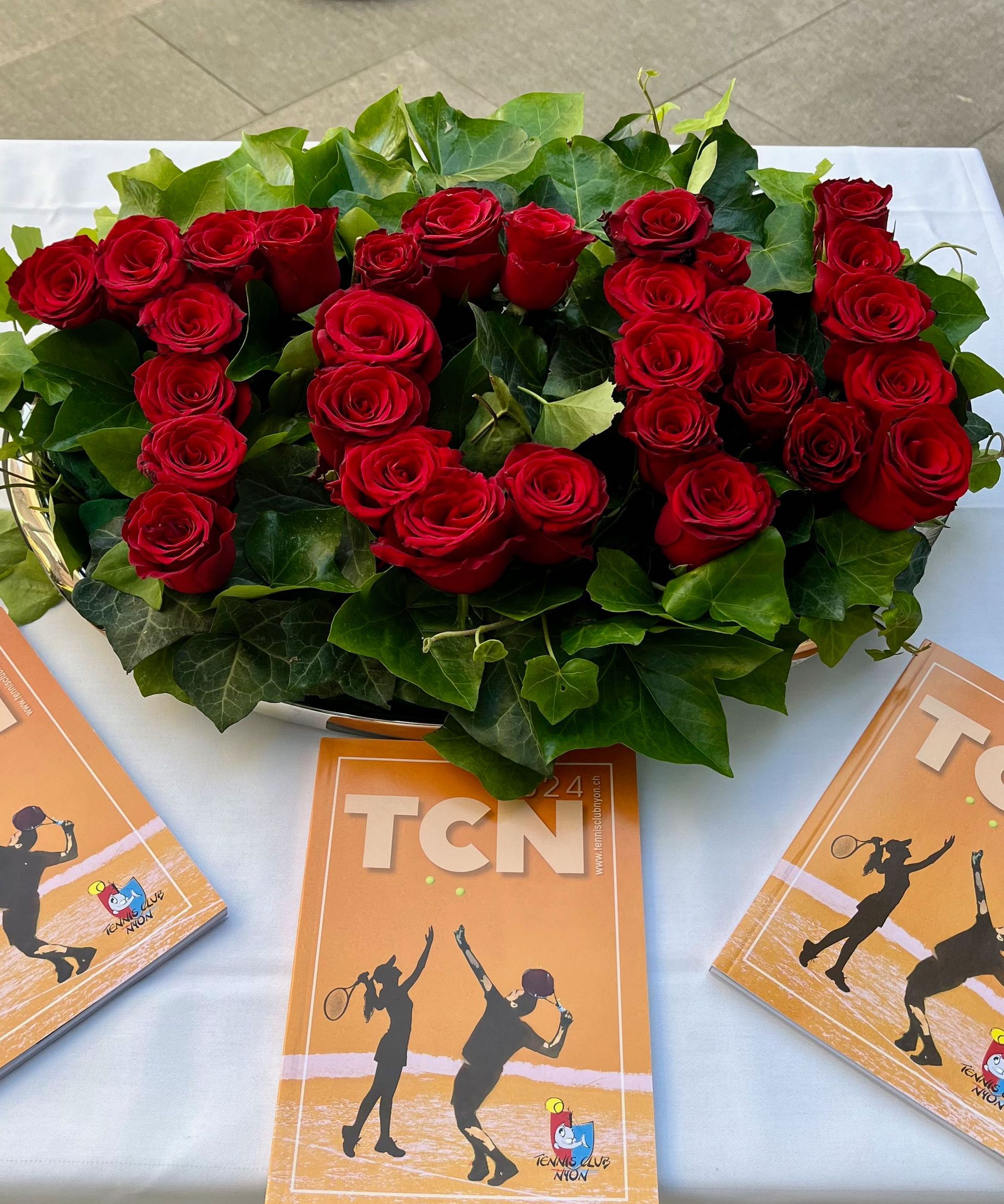 Un bouquet de roses rouges est posé sur une table à côté d'un livre sur lequel est écrit tcn