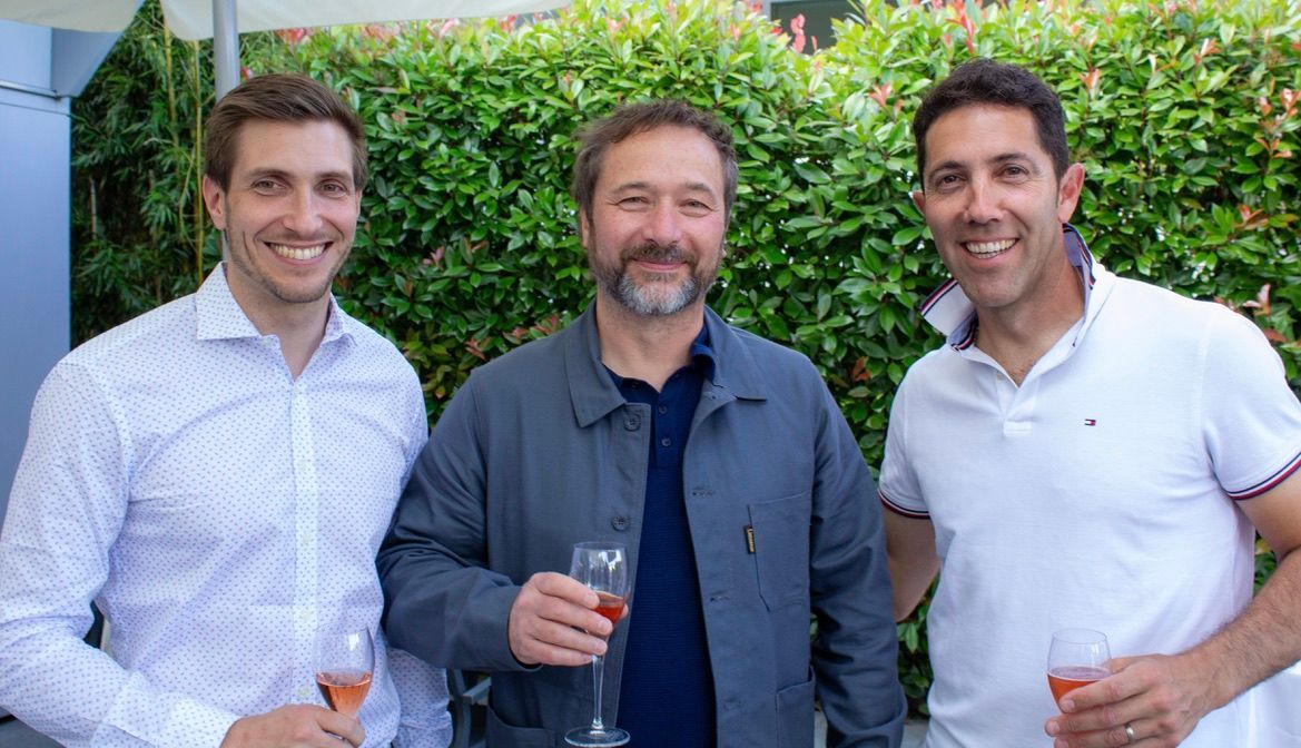 Trois hommes sont debout l'un à côté de l'autre, tenant des verres à vin.