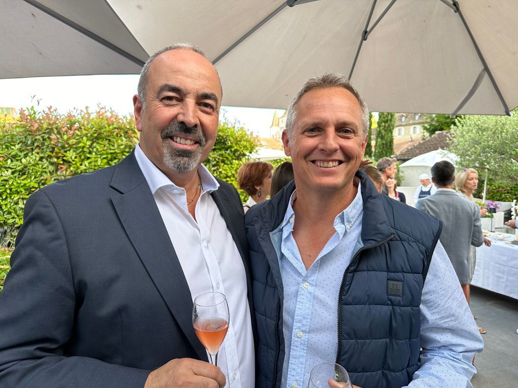 Deux hommes posent pour une photo tout en tenant des verres de vin.