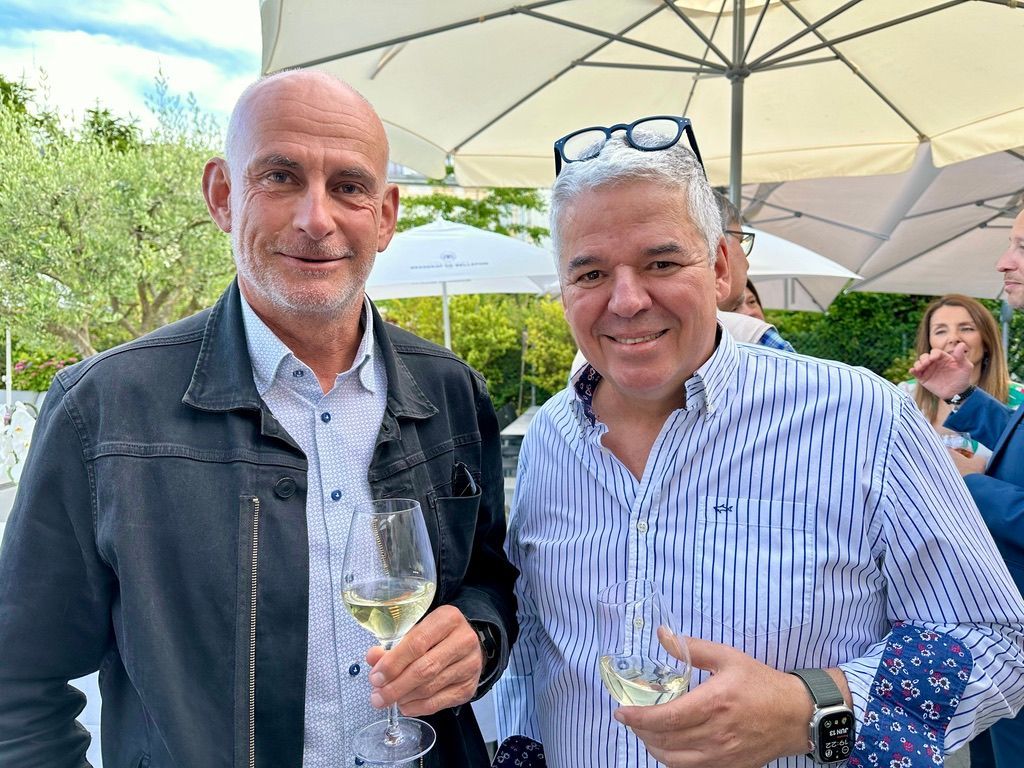 Deux hommes sont debout l'un à côté de l'autre, tenant des verres de vin.