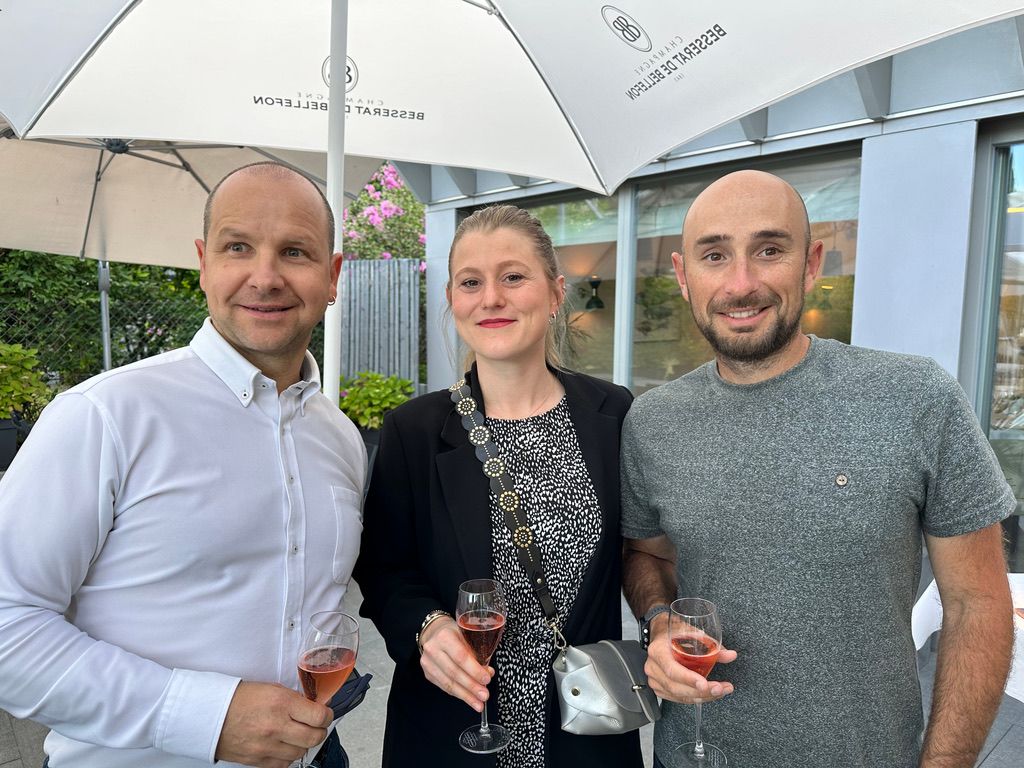 Trois personnes se tiennent côte à côte sous un parapluie tenant des verres à vin.