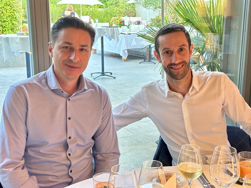 Deux hommes sont assis à une table avec des verres de vin.