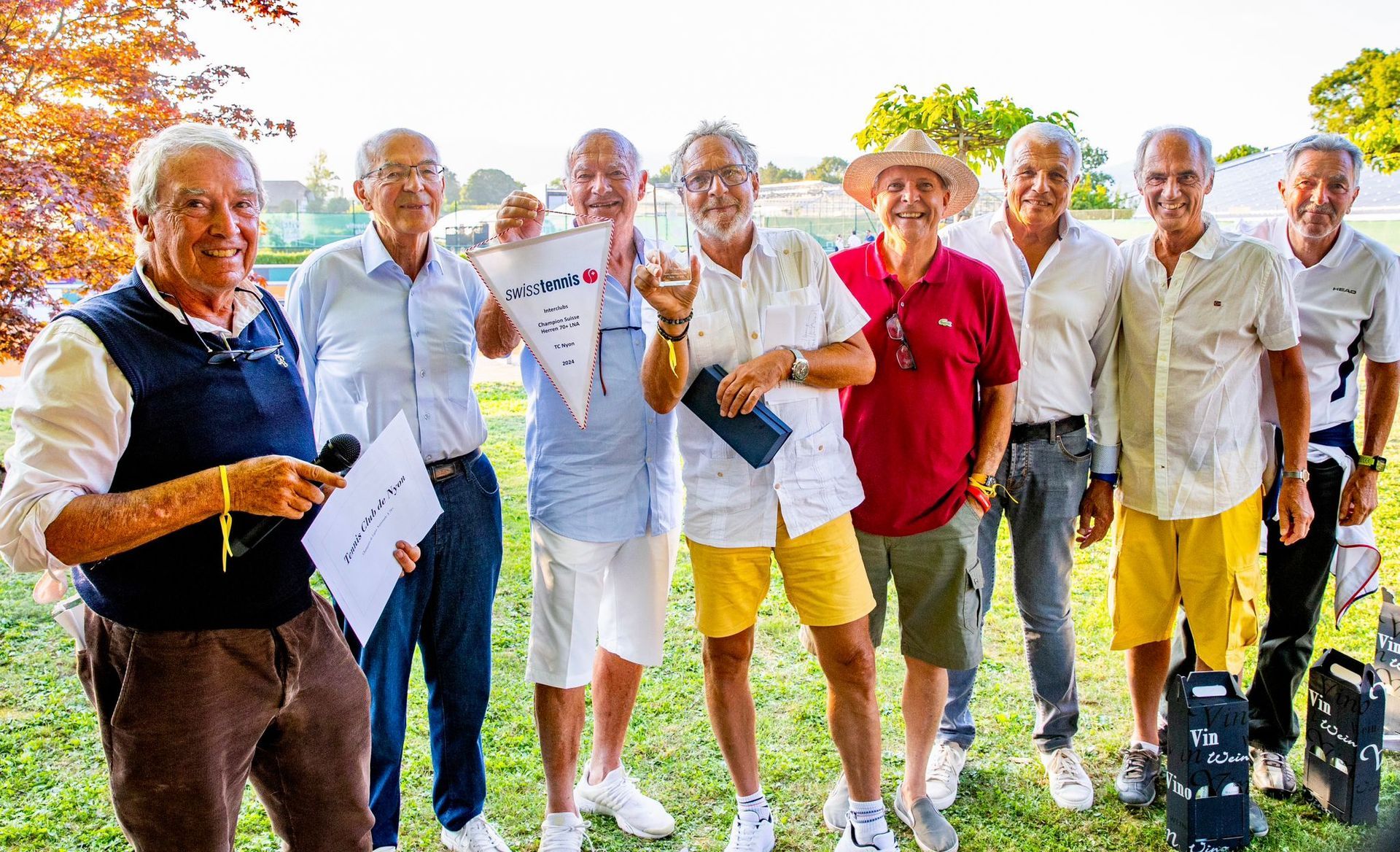 Un groupe d'hommes âgés se tiennent côte à côte dans un champ herbeux.