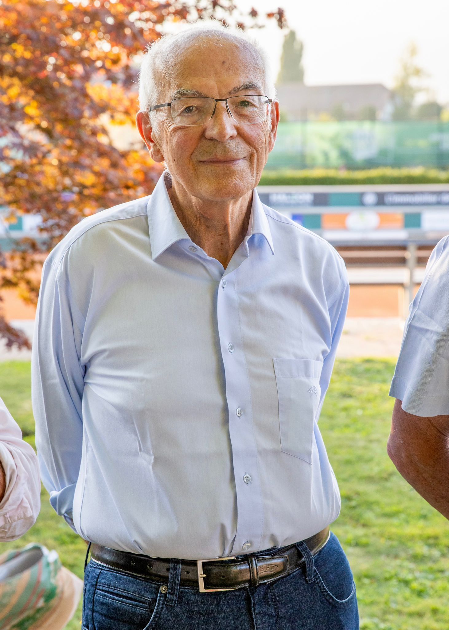 Un homme plus âgé portant des lunettes et une chemise bleue se tient debout dans l'herbe.