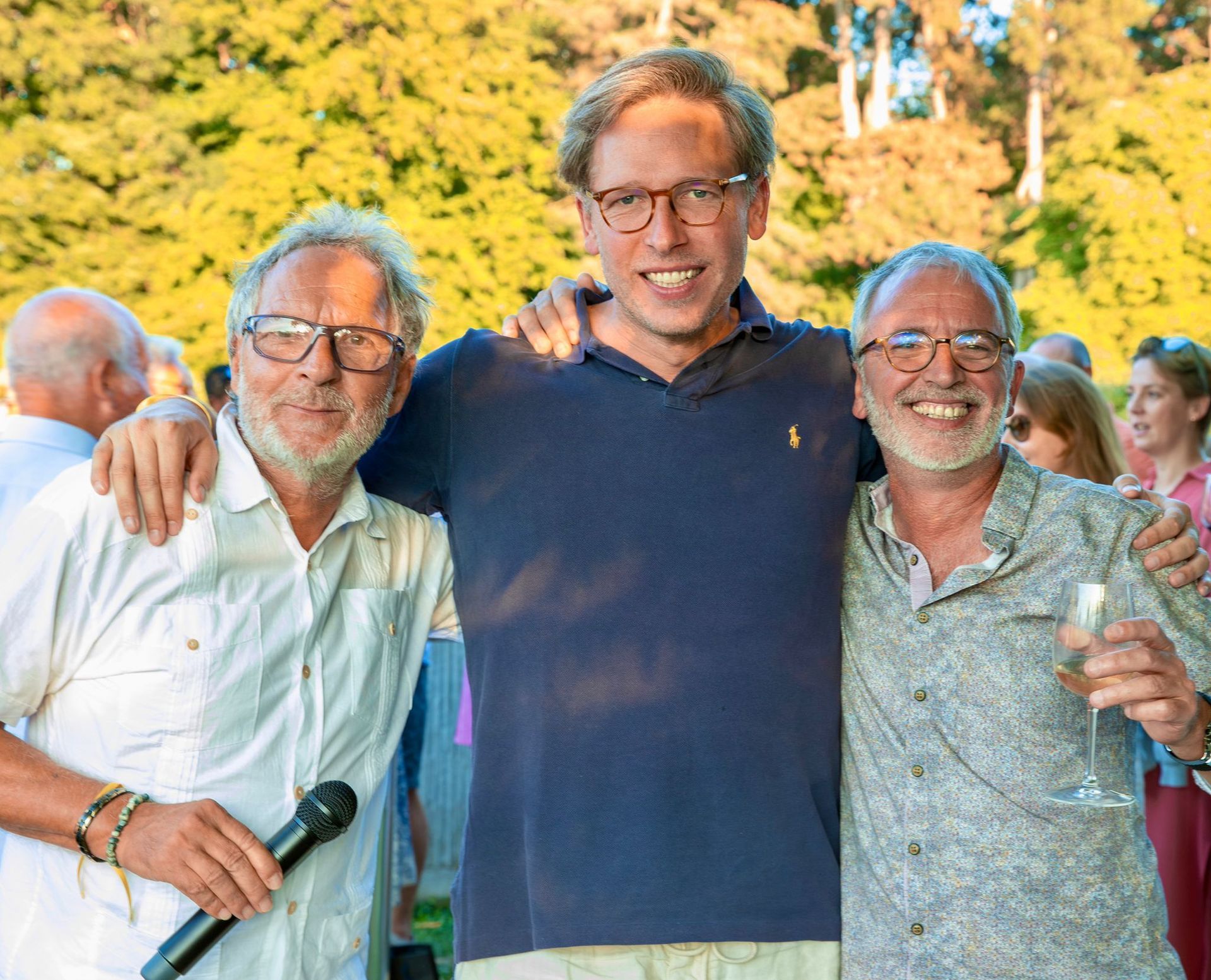 Trois hommes posent pour une photo et l'un d'eux tient un microphone.