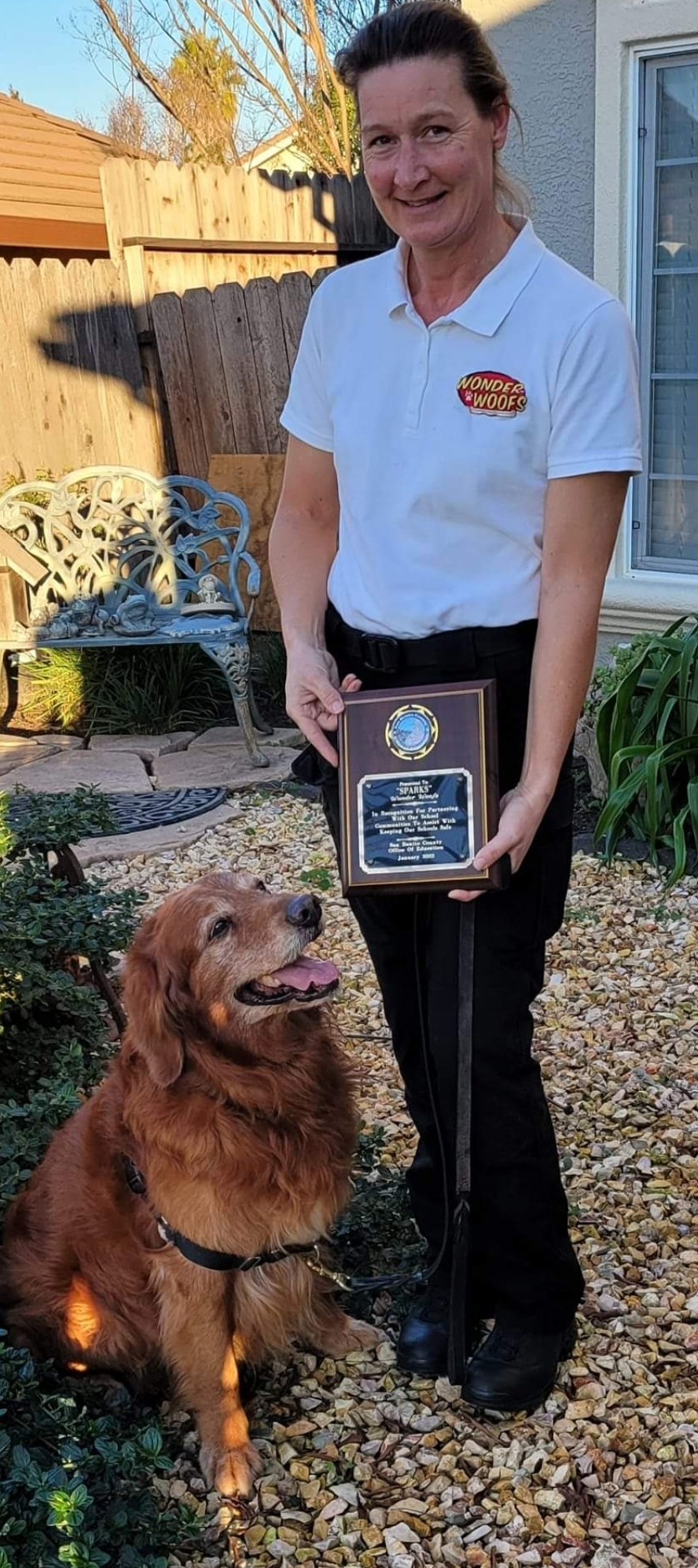 A woman is standing next to a dog holding a plaque.