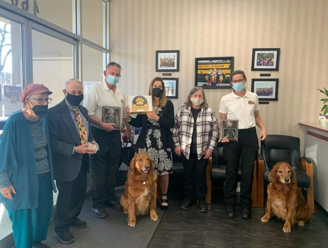 A group of people and two dogs wearing face masks standing in a room.