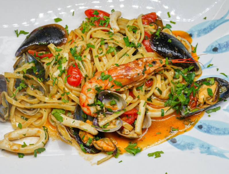 Pasta ai frutti di mare con gamberi, cozze, vongole e pomodori, guarnita con prezzemolo su un piatto bianco.