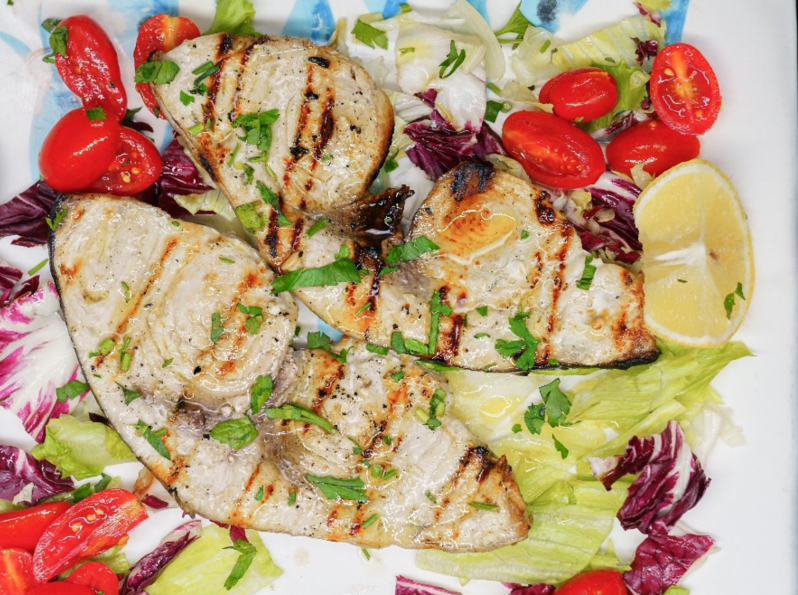 Tranci di pesce alla griglia con pomodorini, limone e insalata.