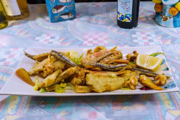 Piatto di pesce fritto con spicchio di limone su un piatto bianco, su una tovaglia a fantasia.