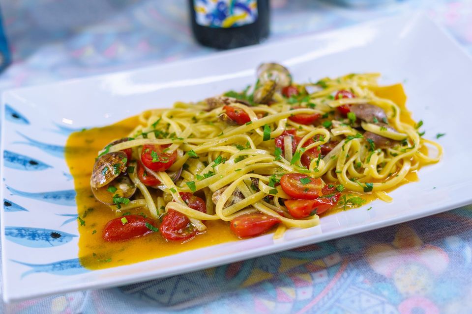 Linguine con pomodorini, pesce e prezzemolo, servite su un piatto bianco decorato con pesci azzurri.
