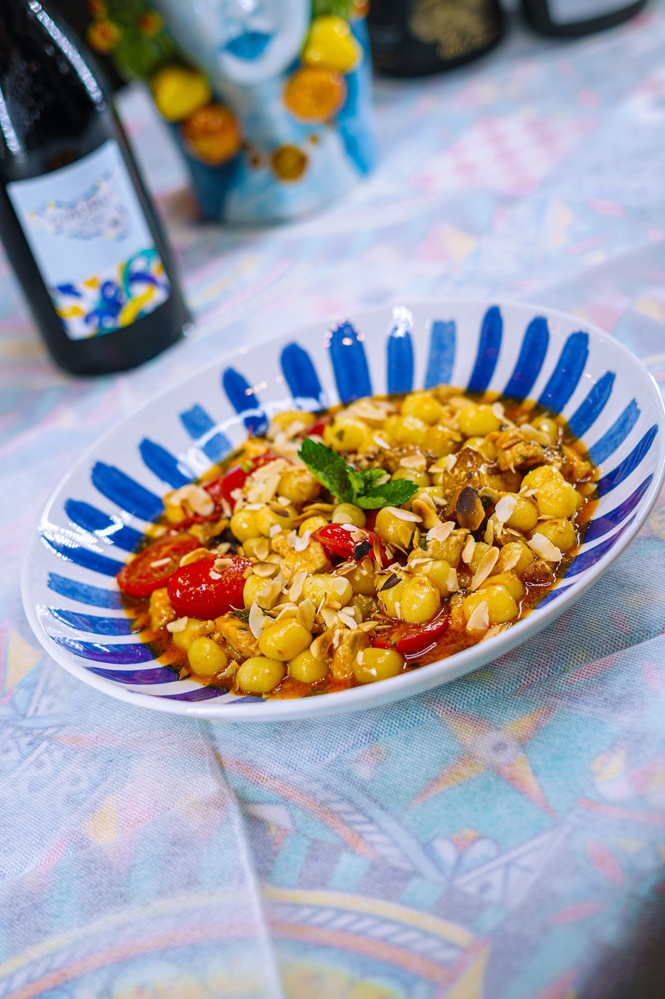 Piatto di gnocchi in una ciotola blu e bianca, con una bottiglia di vino sullo sfondo, su una tovaglia.