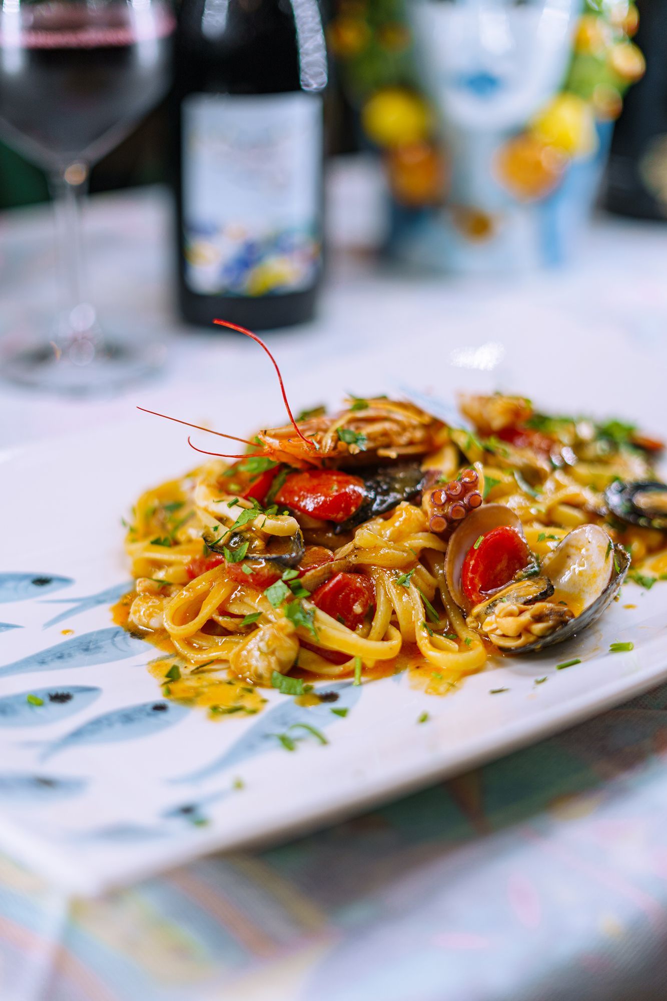 Pasta ai frutti di mare con pomodori ed erbe aromatiche su un piatto bianco, con vino e un secchio sullo sfondo.