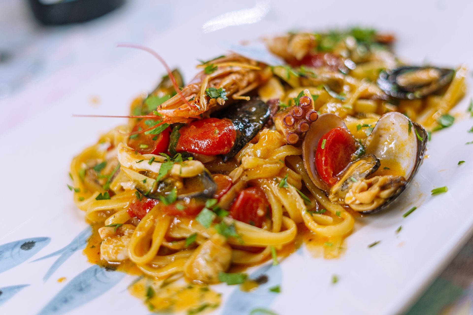 Pasta ai frutti di mare con gamberi, cozze, polpo, pomodori ed erbe aromatiche su un piatto bianco.