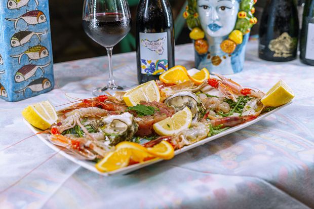 Piatto di frutti di mare con fette di limone e arancia, bicchiere di vino e bottiglie su un tavolo.