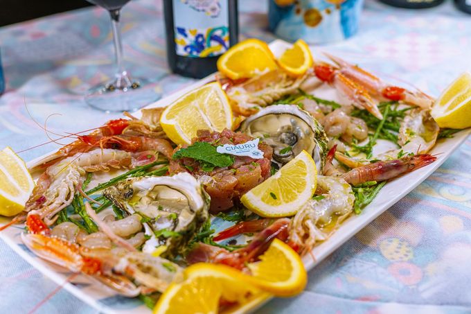 Piatto di frutti di mare con gamberi, ostriche e limoni su un tavolo con vino.