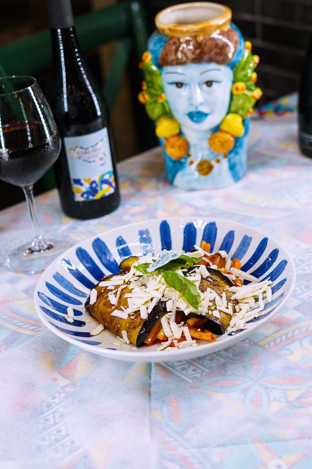 Piatto di melanzane con vino e vaso a forma di testa siciliana.
