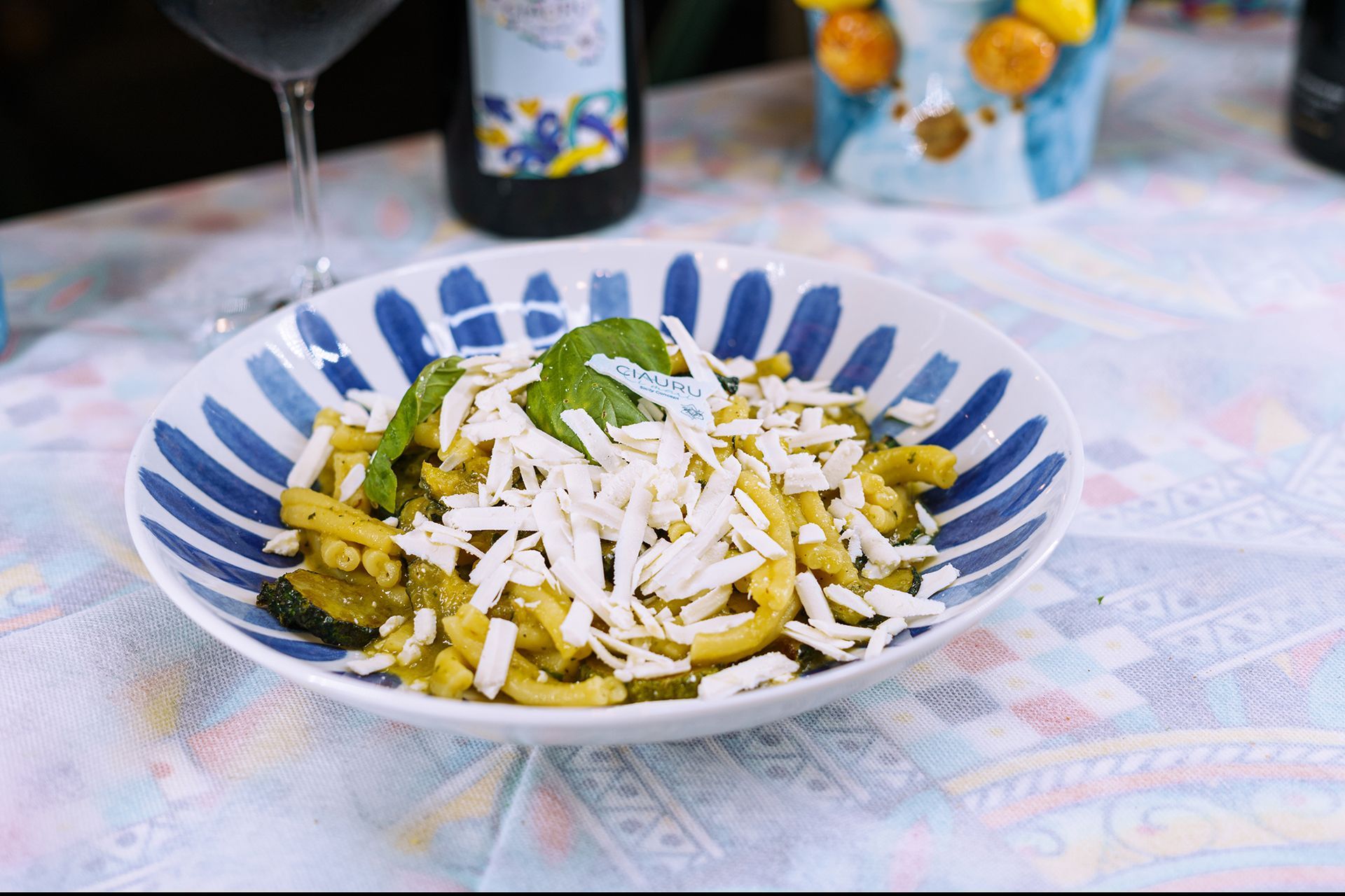 Piatto di pasta con formaggio grattugiato e basilico in una ciotola a righe blu su una tovaglia a fantasia.