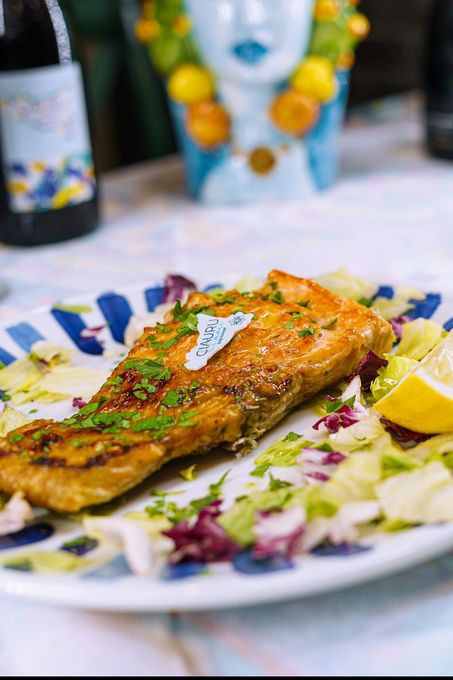 Salmone alla griglia su un piatto con insalata e limone; piatto a strisce blu e bianche.