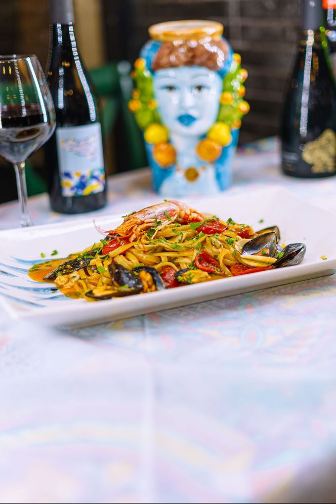 Piatto di pasta con frutti di mare, bicchiere di vino, bottiglie e testa decorativa sul tavolo.