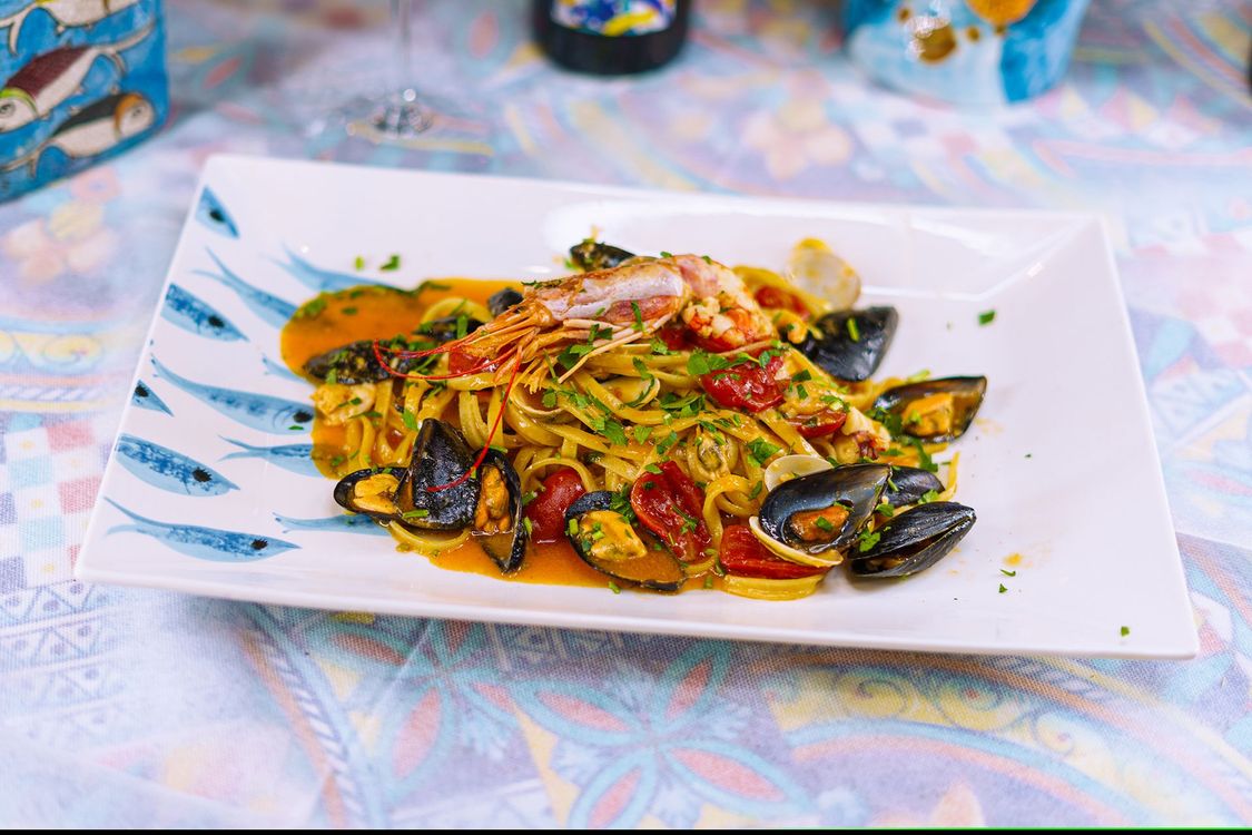 Pasta ai frutti di mare con cozze, gamberi e pomodori su un piatto rettangolare decorato.