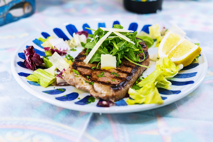 Bistecca alla griglia con rucola, parmigiano e limone su un piatto decorativo.