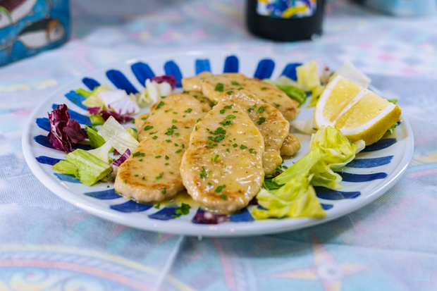 Piatto di pesce cotto con salsa, insalata e spicchio di limone.