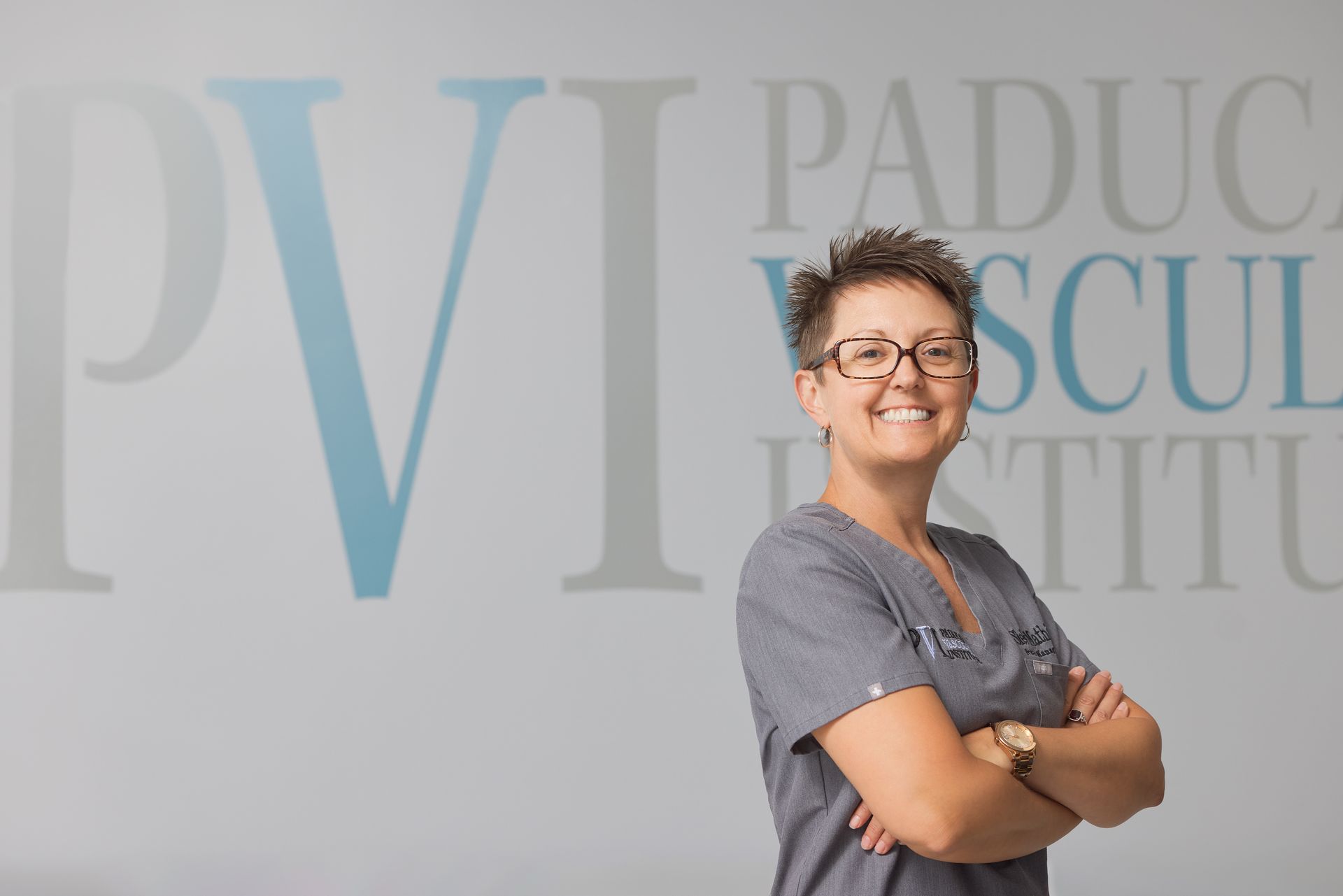 Shelly Mathis, PVI Practice Manager. A woman in scrubs stands with her arms crossed in front of a pv institute sign.