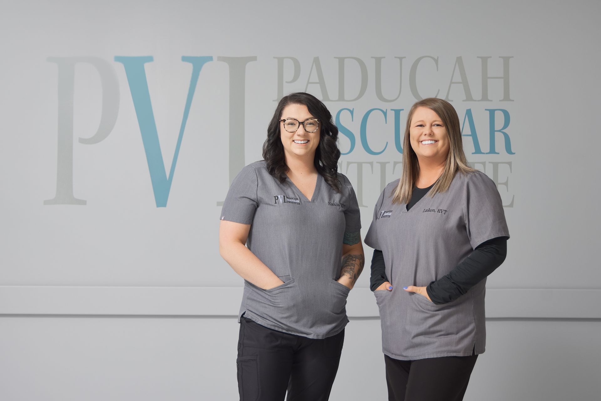 Two women in scrubs are standing next to each other in front of a wall.