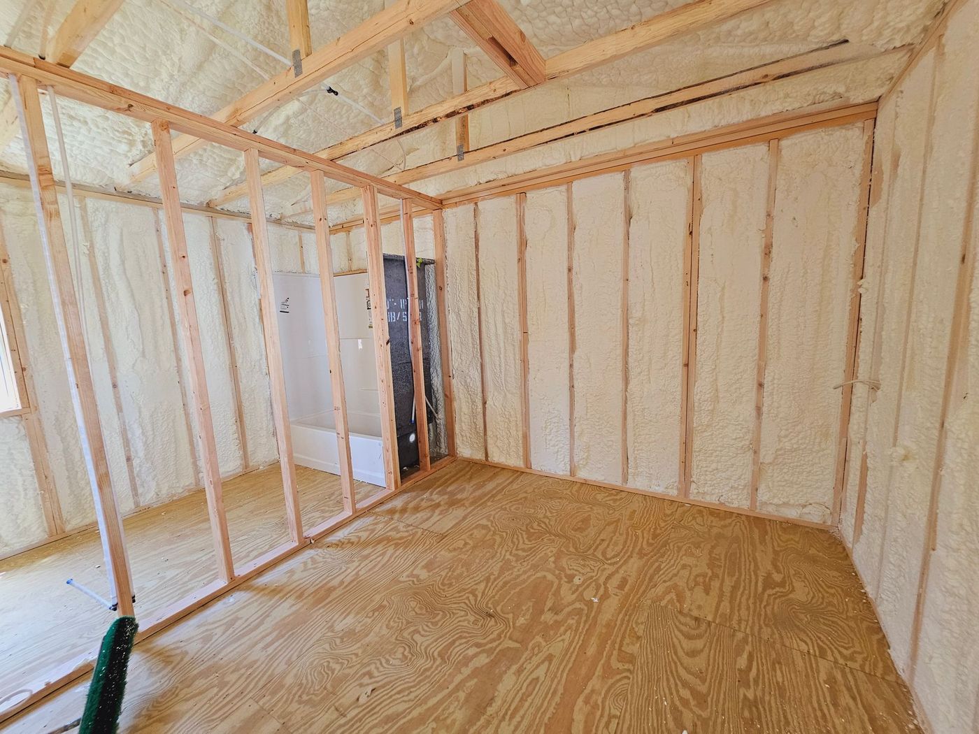 A room with wooden walls and a wooden floor is being insulated with spray foam.