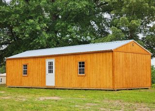 A large wooden building with a metal roof is sitting in the middle of a grassy field.