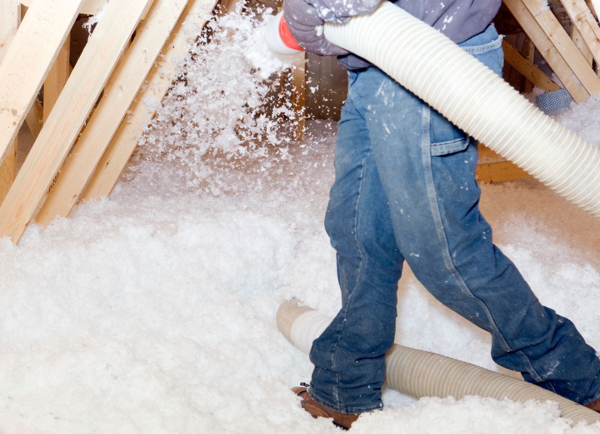 A person is blowing insulation into an attic with a hose